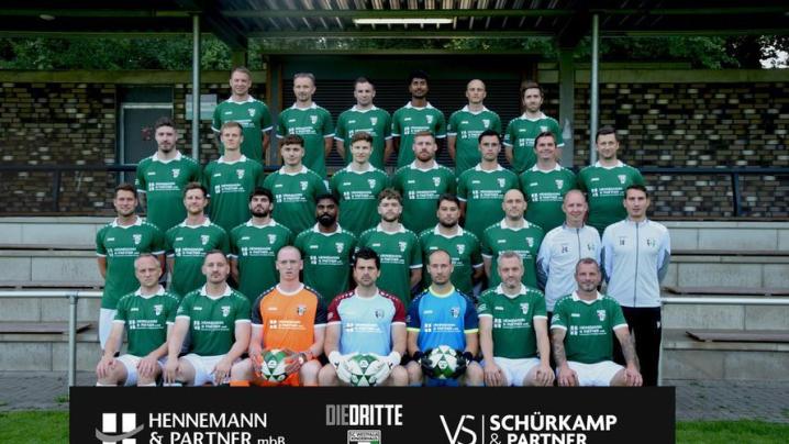 Großes Teamfoto von Fußballspielern, die vor einem Sportgebäude posieren.