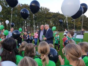Eine Gruppe von Menschen steht auf einem Sportfeld vor einem Hintergrund mit vielen Ballons.