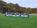 Eine Gruppe von Menschen hält auf einem grünen Sportfeld verschiedene Vereinsflaggen vor einem Hintergrund aus Bäumen.
