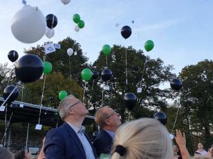Menschen beobachten bunte Ballons, die an einem hellblauen Himmel schweben.