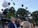 Menschen beobachten bunte Ballons, die an einem hellblauen Himmel schweben.