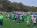 Eine große Gruppe von Kindern in Sportuniformen steht auf einem grünen Fußballfeld vor einem bewaldeten Hintergrund.
