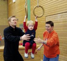 Eine Familie mit einem kleinen Kind und einem Jungen in einer Sporthalle mit Trainingsringen.