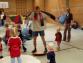 Eine große Gruppe von Kindern und Erwachsenen in einer Sporthalle, die an einer kooperativen Spiel- oder Lernaktivität teilnehmen.