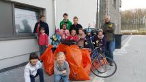 Eine Gruppe von Erwachsenen und Kindern steht vor einem modernen Gebäude und ist umgeben von mehreren großen orangefarbenen Säcken.