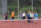 Gruppe von Kindern beim Spielen von Sportarten wie Tennis auf einem roten Sportplatz.