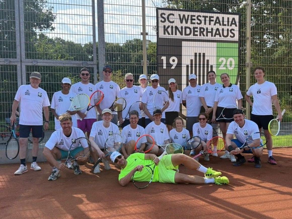 Eine sportliche Gruppe vor dem Vereinsnamen SC Westfalia Kinderhaus auf einem Tennisplatz.