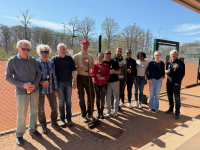 Eine Gruppe von Männern steht im Freien vor einer Sportanlage und posiert für ein Gruppenfoto.