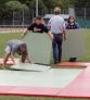 Mehrere junge Personen tragen und bearbeiten große, rechteckige Platten im Freien auf einem Sportplatz.