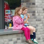 Zwei junge Mädchen sitzen auf einer Mauer vor einem Geschäft und essen Eis.