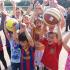 Eine Gruppe von Kindern und Erwachsenen spielt bei einem sportlichen Event draußen mit verschiedenen Sportbällen.