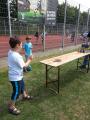 Ein Junge steht auf einer Rasenfläche vor einer Sportanlage, auf der ein langer Holztisch platziert ist.