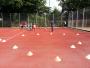 Sportplatz mit roten Bodenbelägen, auf dem mehrere Personen spielen und orangefarbene Trainingskonen verteilt sind.