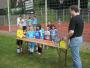 Eine Gruppe junger Jungen in Sportkleidung steht hinter einem Tisch auf einem Sportplatz, neben ihnen steht ein erwachsener Mann.