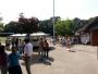 Eine belebte Szene in einem Park oder auf einem Jahrmarkt mit vielen Menschen und Verkaufsständen.