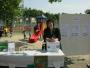 Eine Frau sitzt an einem Informationsstand im Freien, der Broschüren zu einem Vereinsheim und Freizeitaktivitäten ausgibt.