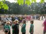 Eine große Gruppe von Kindern in Sportkleidung steht auf einem grünen Sportplatz unter vielen Bäumen.