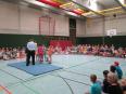 Innenansicht einer großen Sporthalle, die bei einer Gemeinschaftsveranstaltung von vielen Menschen besucht wird.