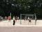 Mehrere Kinder und Jugendliche spielen Fußball vor einem Tornetz auf einem Sportfeld.