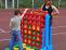 Ein Junge und eine Frau interagieren vor einer großen, roten Spielstation auf einem Sportplatz.