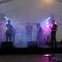 Eine Band spielt live auf einer beleuchteten Bühne unter einem Zelt.