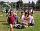 Eine Gruppe von Familien spielt in einem grünen Park bei Sonnenschein, wobei ein großer bärenartiger Spielbogen im Vordergrund zu sehen ist.