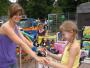 Zwei Mädchen stehen auf einem Jahrmarkt: Die ältere lächelt und hält die Hand der jüngeren.