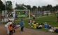 Eine Gruppe von Menschen spielt auf einem Sportplatz, wobei Kinder einen großen Springstall nutzen und andere im Freien entspannen.