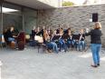 Eine Gruppe von Musikern, darunter Kinder und Erwachsene, übt draußen mit Violinen und Musikinstrumenten vor einem modernen Gebäude.