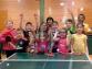 Eine Gruppe lächelnder Kinder posiert zusammen hinter einem Tisch mit Netz, der für Tischtennis verwendet wird.
