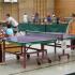 Innenaufnahme einer Sporthalle mit mehreren aufgebauten Tischtennisplatten, an denen Kinder und Erwachsene spielen.