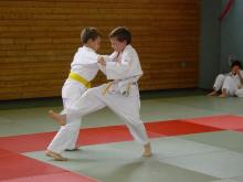 Zwei junge Jungen in weißen Kampfkleidern üben eine martialistische Technik in einem Dojo.