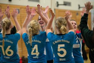 Eine Gruppe jubelnder junger Sportlerinnen mit blauen Trikots in einer Sporthalle.