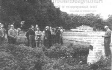 Eine historische Schwarz-Weiß-Aufnahme einer Gruppe von Menschen, die in einer grünen Außenanlage vor einem Gebäude posieren.