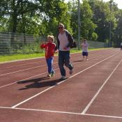 Familie joggt auf einer roten Laufbahn mit grünem Waldhintergrund.