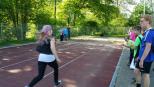 Eine Frau läuft über einen Sportplatz, begrenzt durch einen Park mit viel Grün.