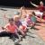 Eine Gruppe spielender Kinder und eine erwachsene Frau sind im Freien auf Pflastersteinen zu sehen.