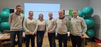 Eine Gruppe von Personen posiert in einem modernen Konferenzraum vor einem Projektionsbildschirm.